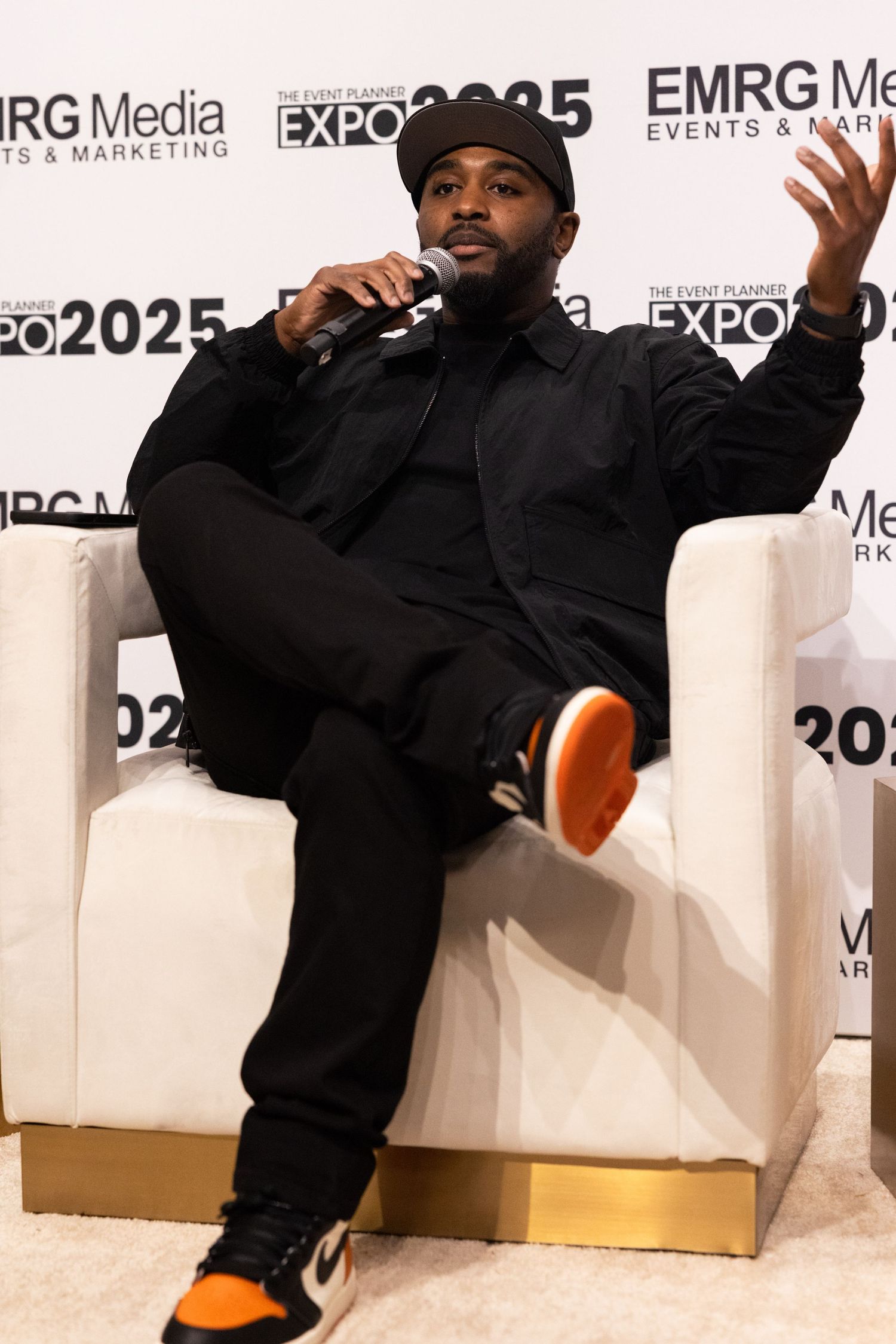 Person in black clothing performs energetic breakdancing moves on white floor at media expo event.