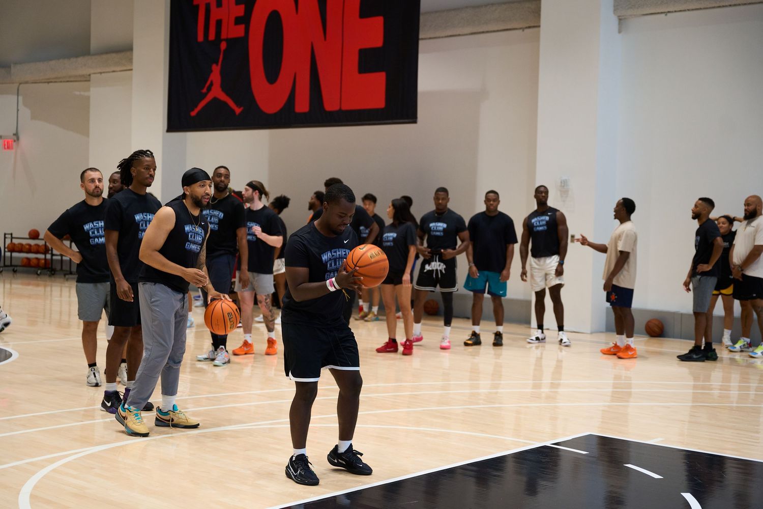 Basketball players compete during a training session in an indoor gym with the word 'ONE' displayed on the wall.