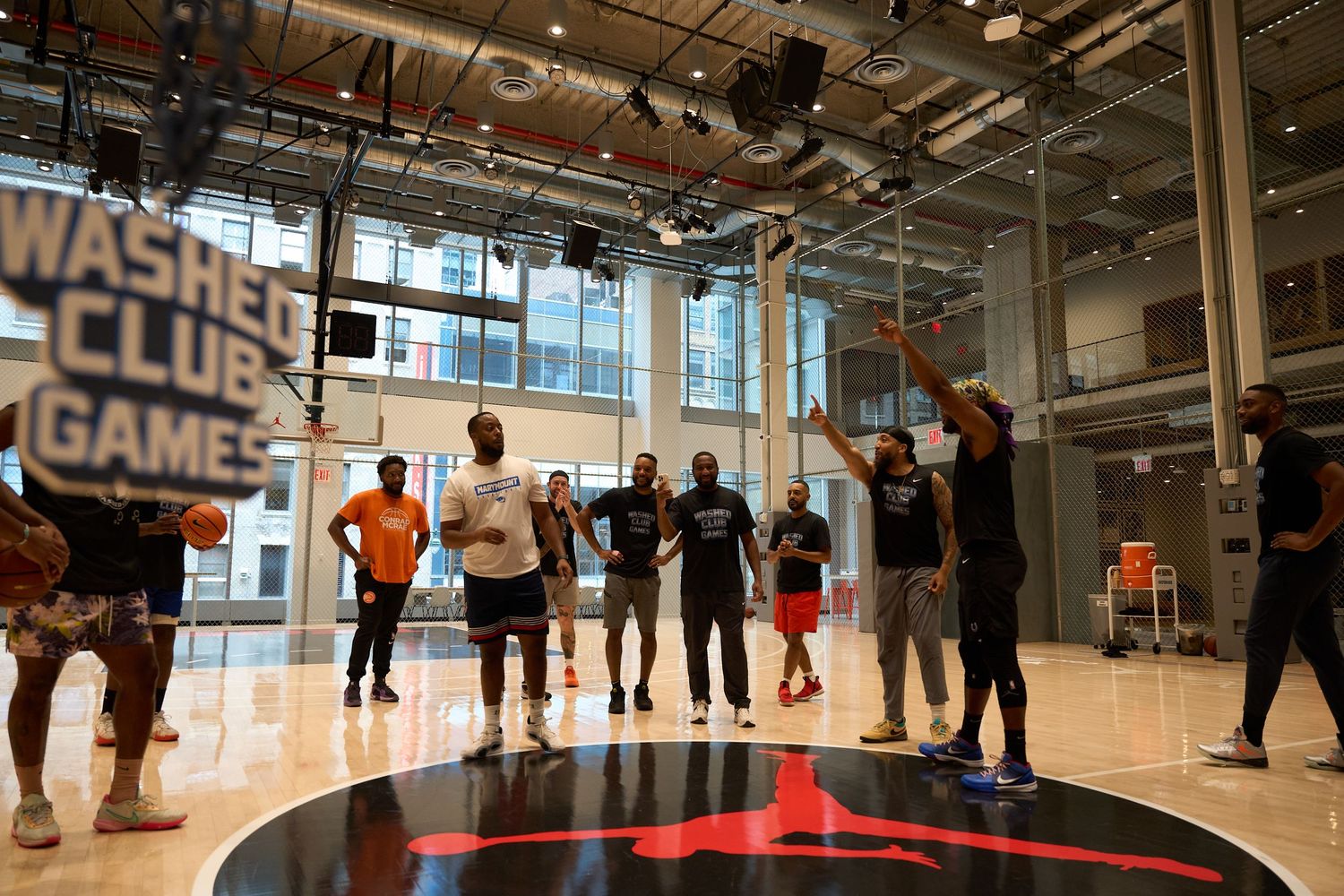 Players gathering in a large indoor gymnasium space with bright lighting and training equipment visible.