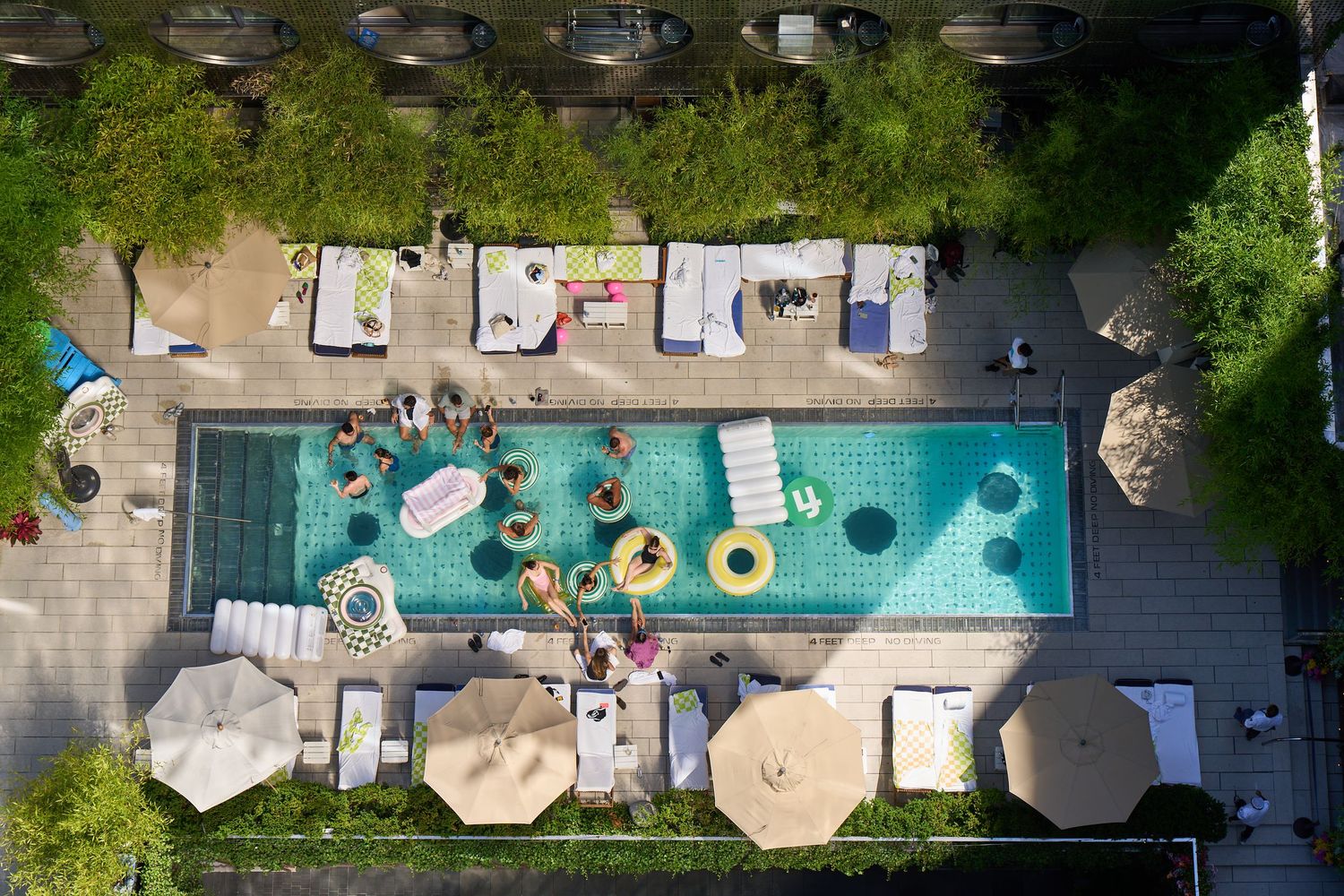 Aerial view of resort hotel swimming pools with colorful floats and lounge chairs arranged around aqua blue water.