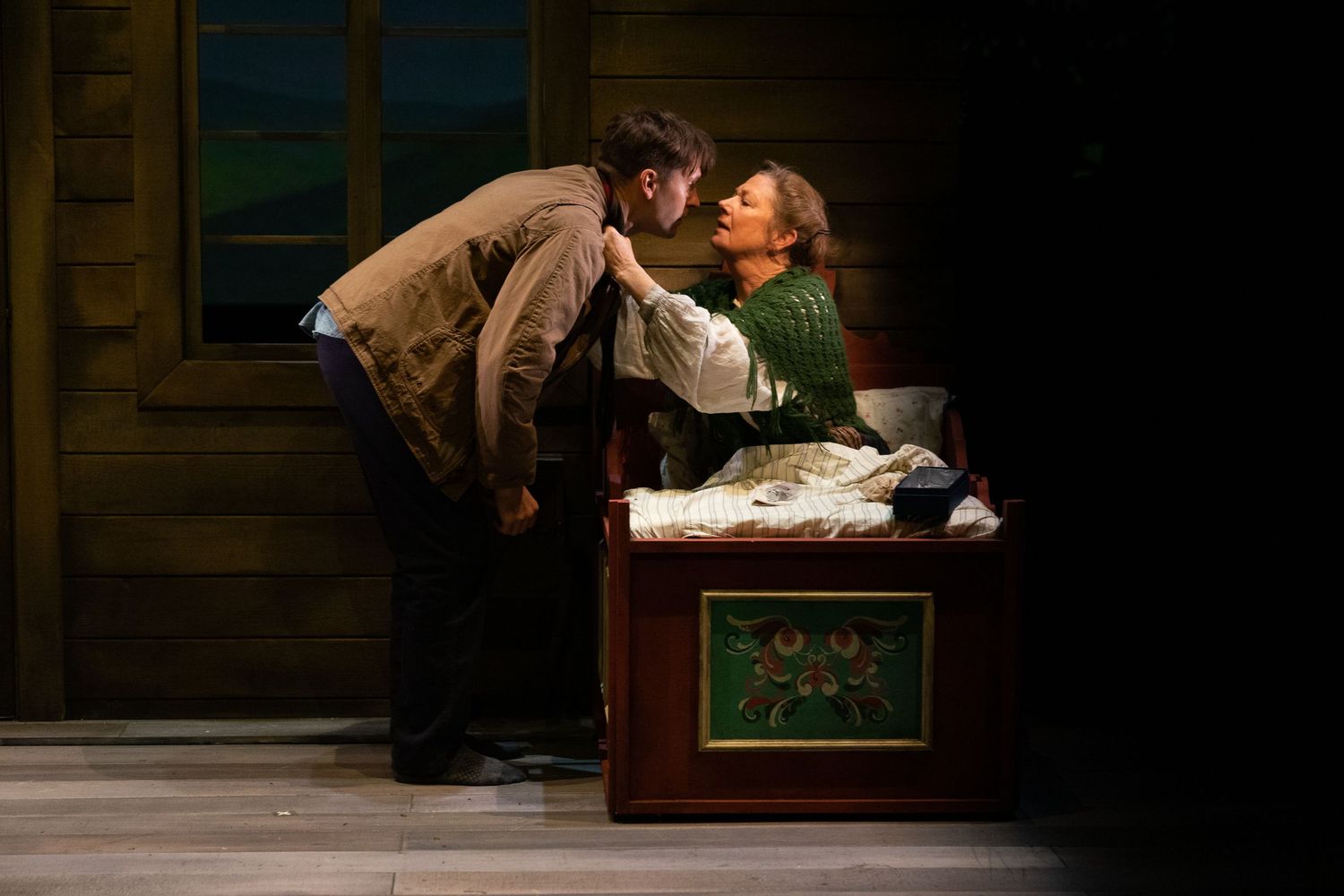 A couple in historical period costumes embrace and interact intimately on an antique-style bed during a theatrical performance.