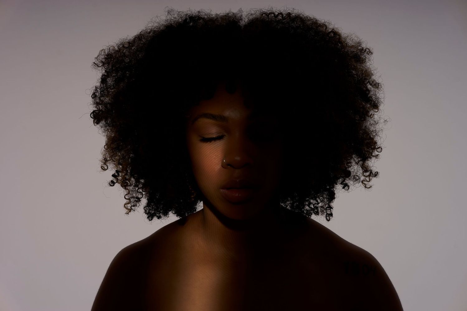 Silhouetted figure with natural curly afro hair against dramatic backlit background.