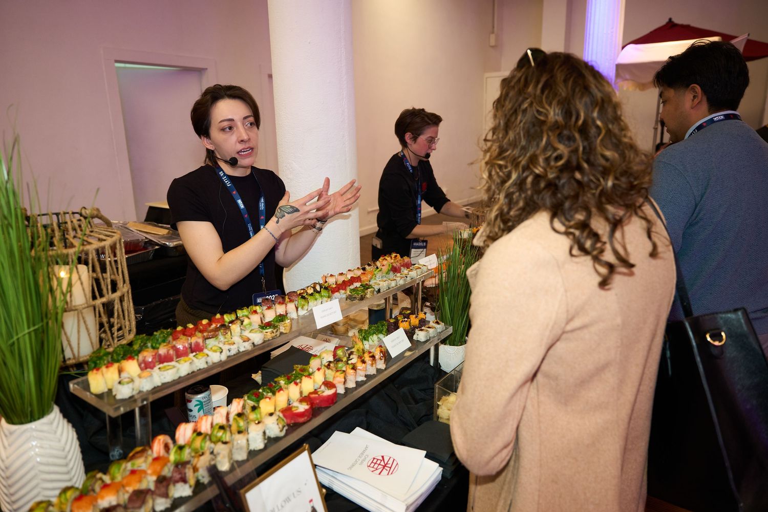People gather around a long table filled with colorful sushi rolls and appetizers at an elegant event.