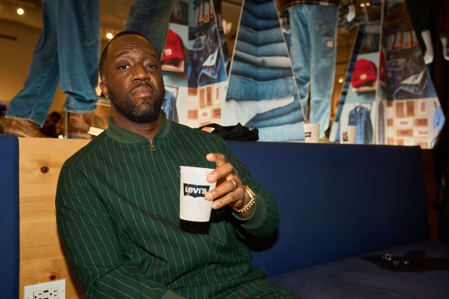A person in a dark green sweater smiles while holding a beverage in a dimly lit setting.