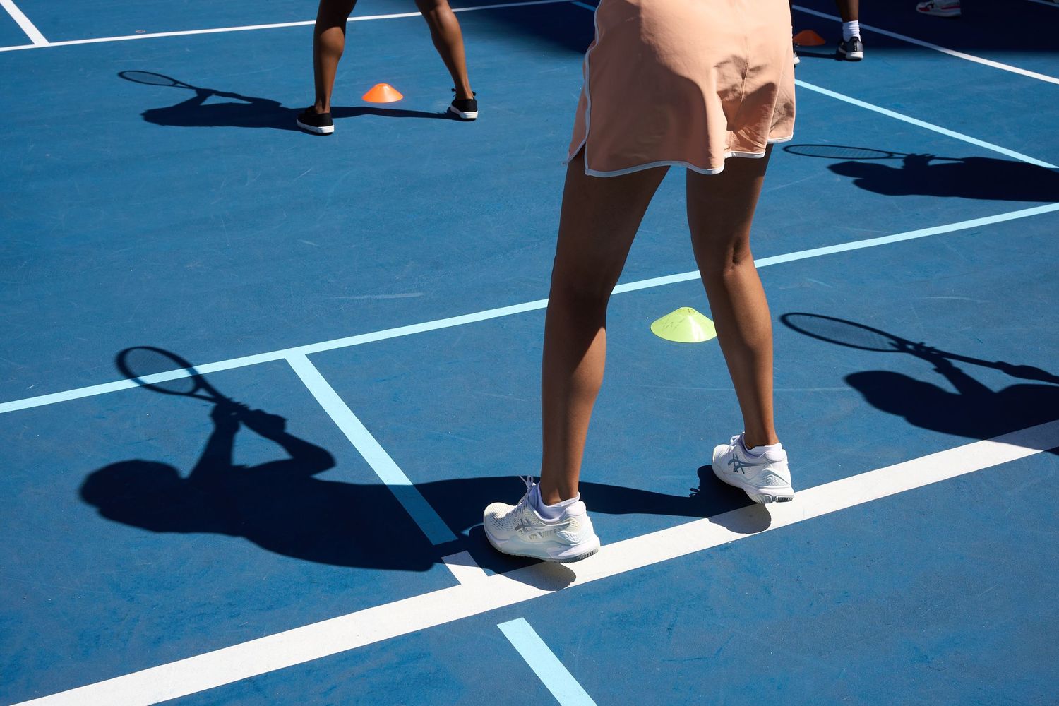 Tennis players positioned on blue courts during a training session.