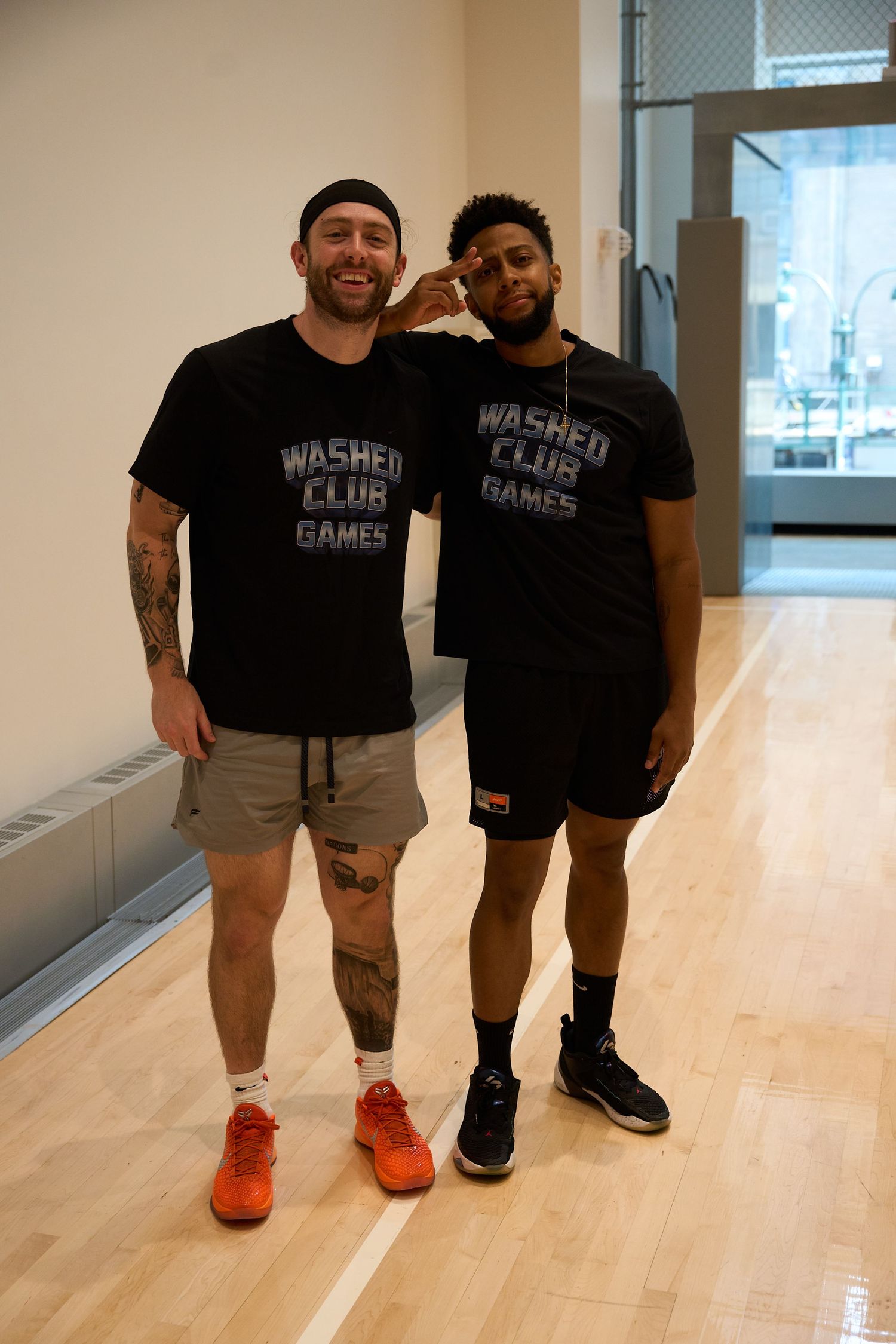 Players in matching black shirts stand together on a wooden basketball court during a training session.