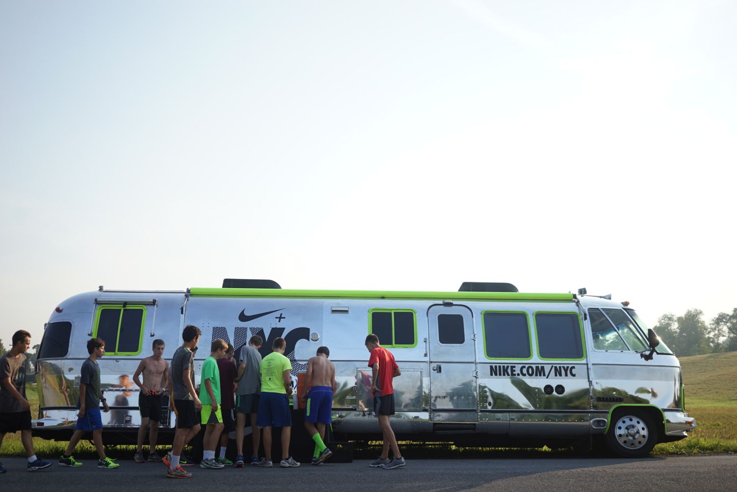 A white and lime green party bus parked on grass with people gathering around it at an outdoor event.
