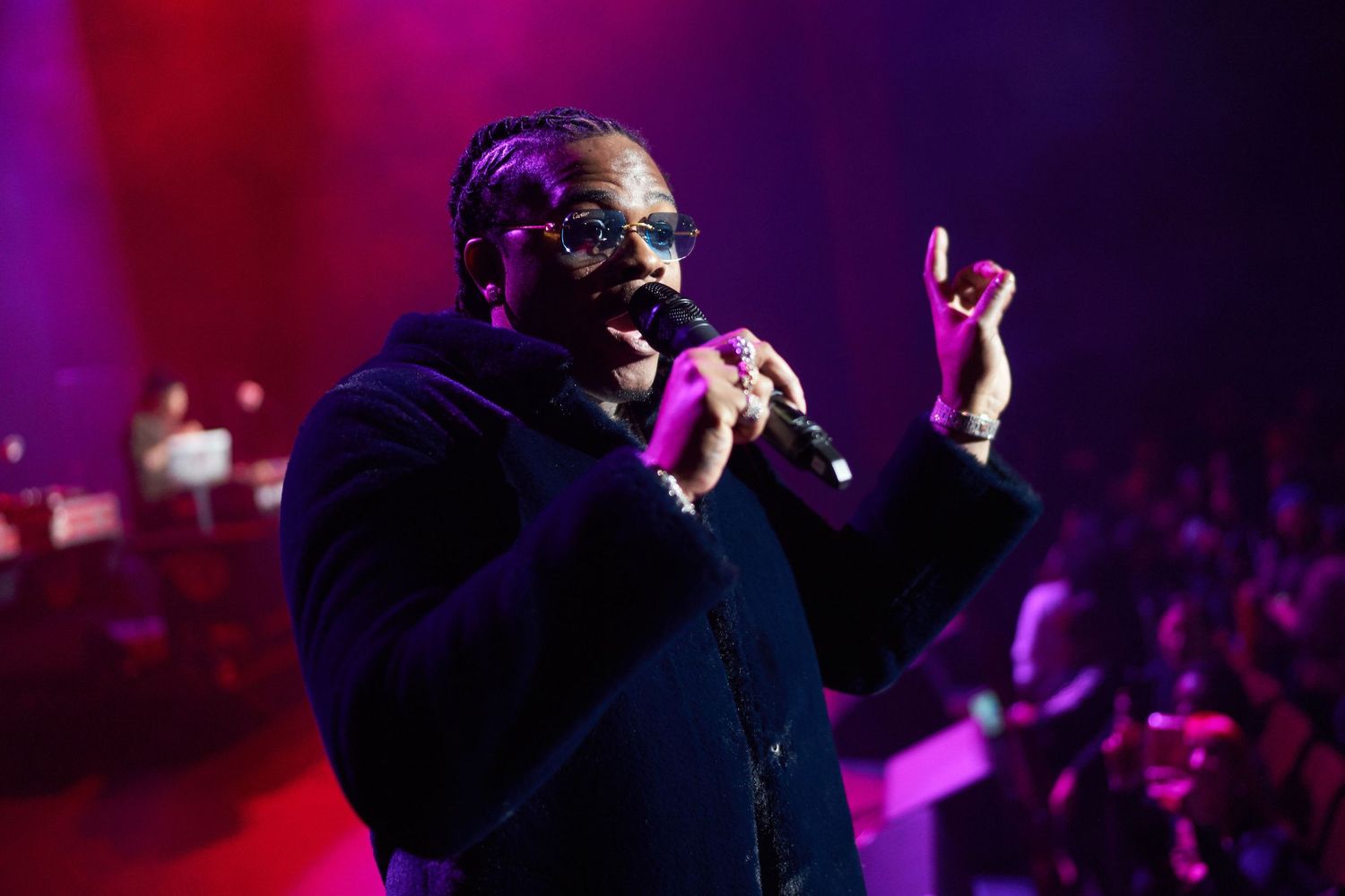 An entertainer performs on stage in purple lighting holding a microphone and gesturing to the enthusiastic crowd.