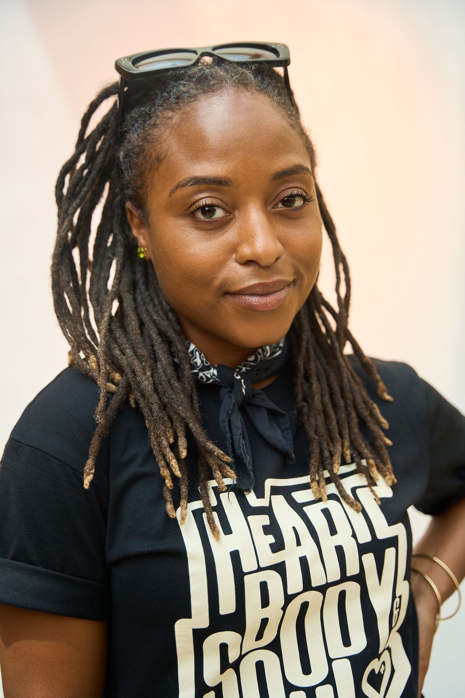 Woman with locs and sunglasses on head wearing a black I Heart Books t-shirt smiling at camera.