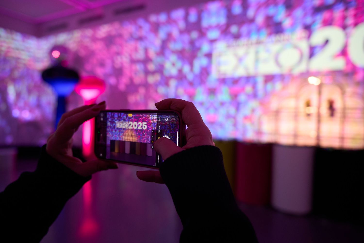Silhouetted hands holding phones to record a concert with vibrant purple and pink stage lighting in the background.