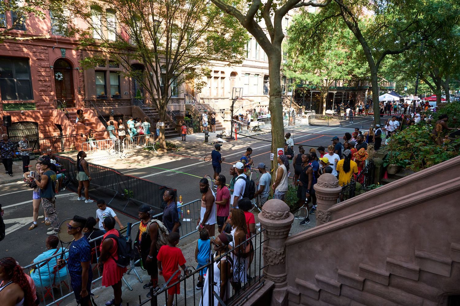 Crowd of people queuing along a residential street with brick buildings and trees.
