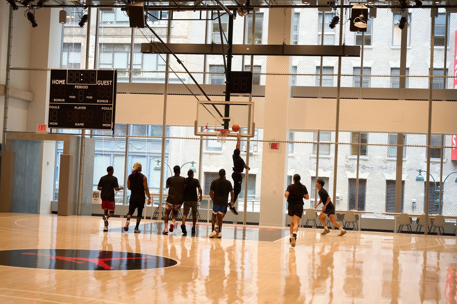 Large empty gymnasium space with high windows and polished floors showing basketball courts and scattered players.