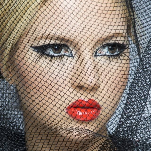 Dramatic beauty portrait through black fishnet veil showing bright red lipstick and smoky eye makeup.