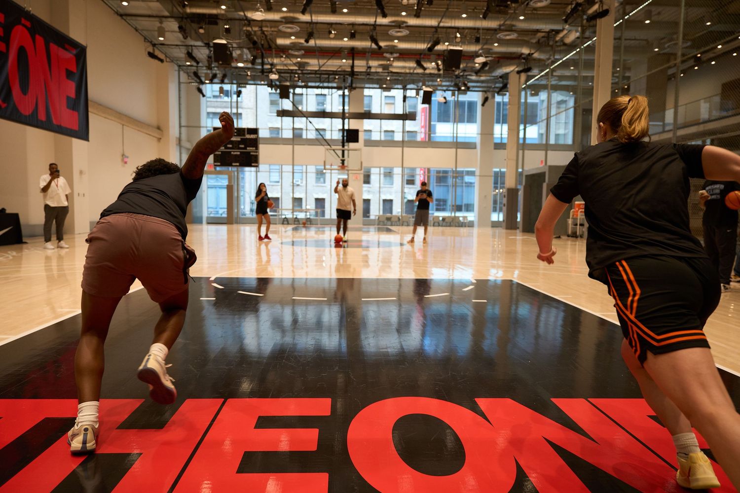 Fitness enthusiasts train in a modern gym space with red flooring and large windows letting in natural light.