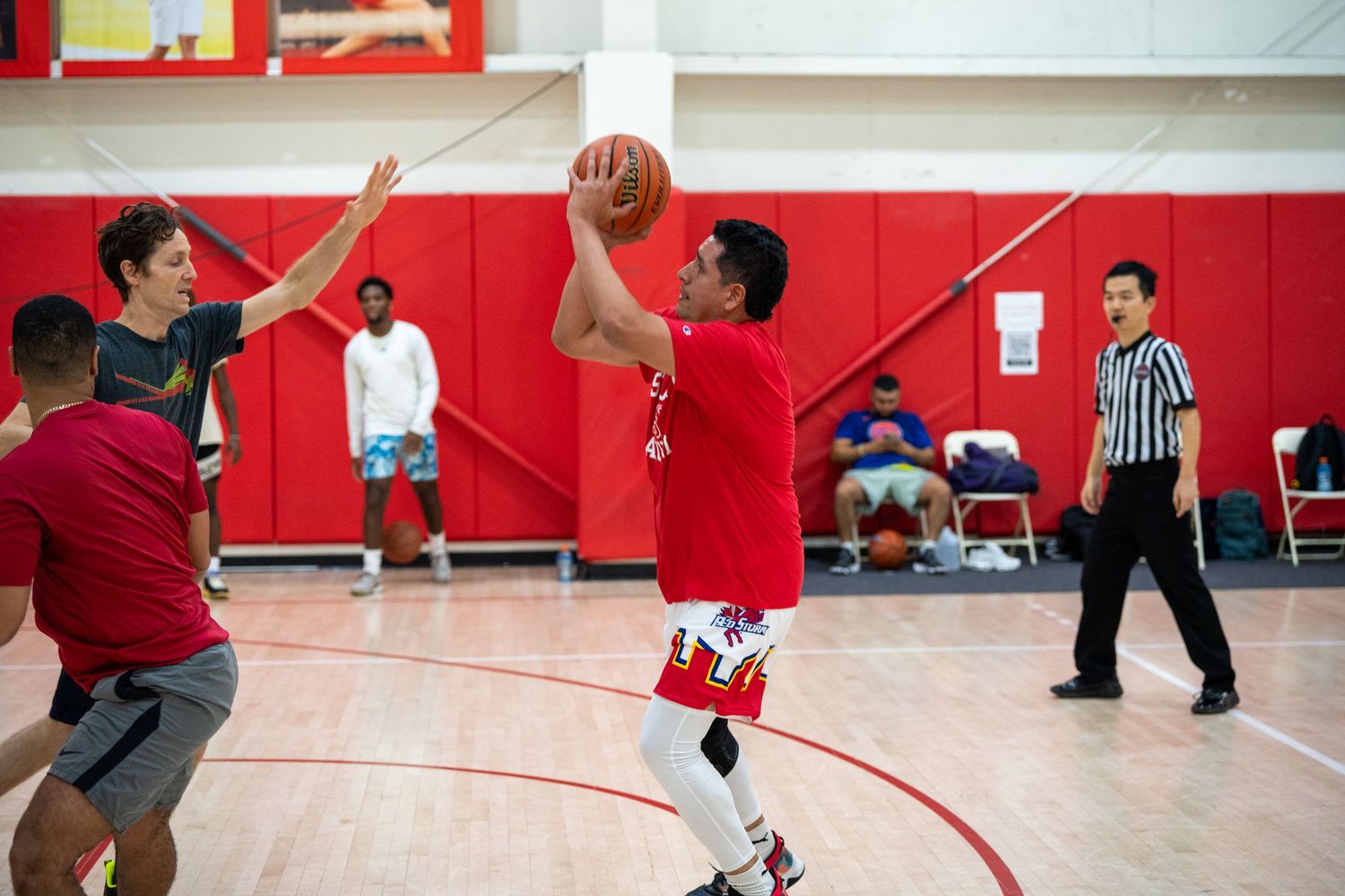 Basketball players compete in a red-walled gymnasium during an indoor game.