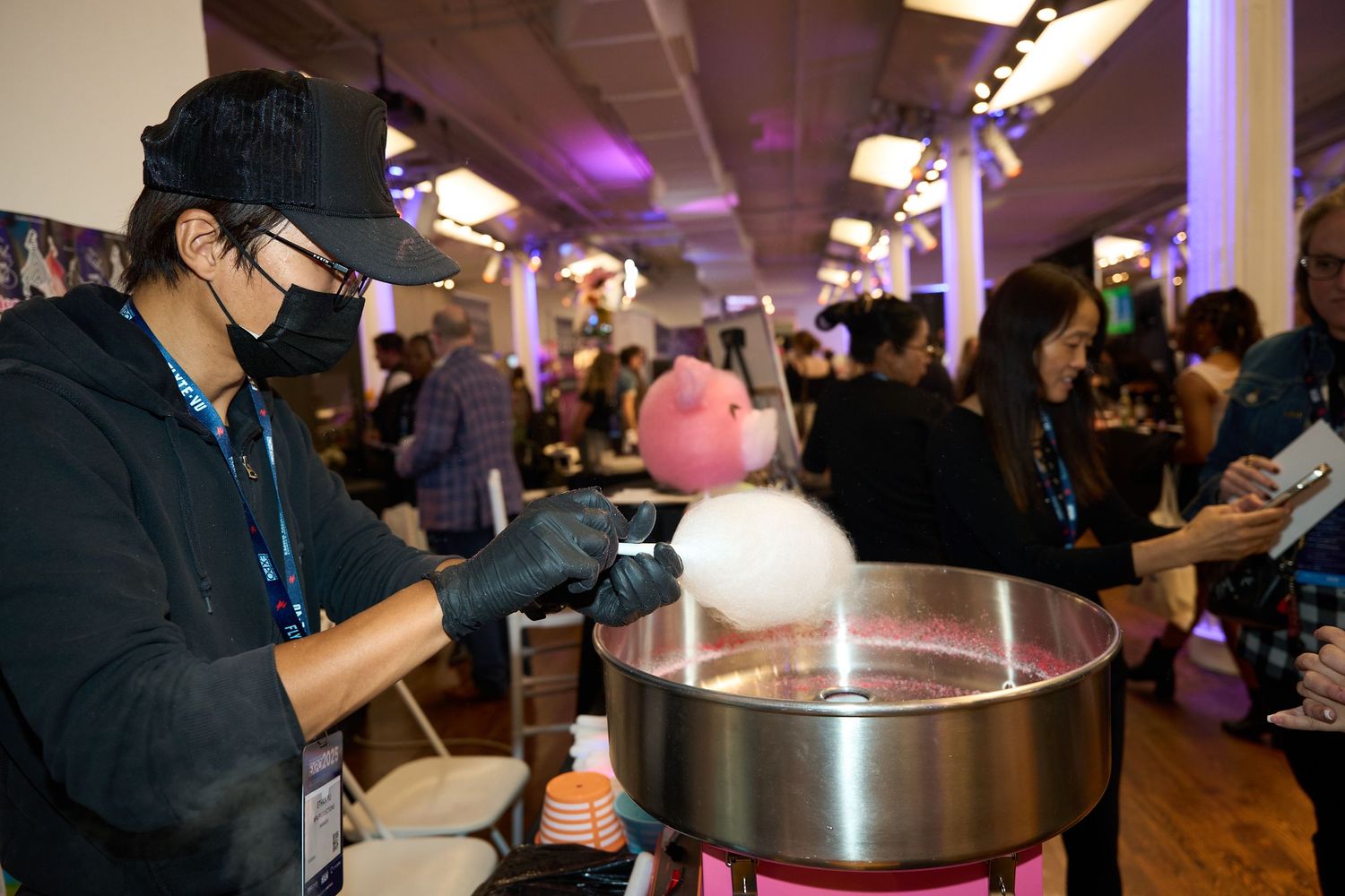 A series of people preparing cotton candy at a crowded indoor event using professional spinning machines.