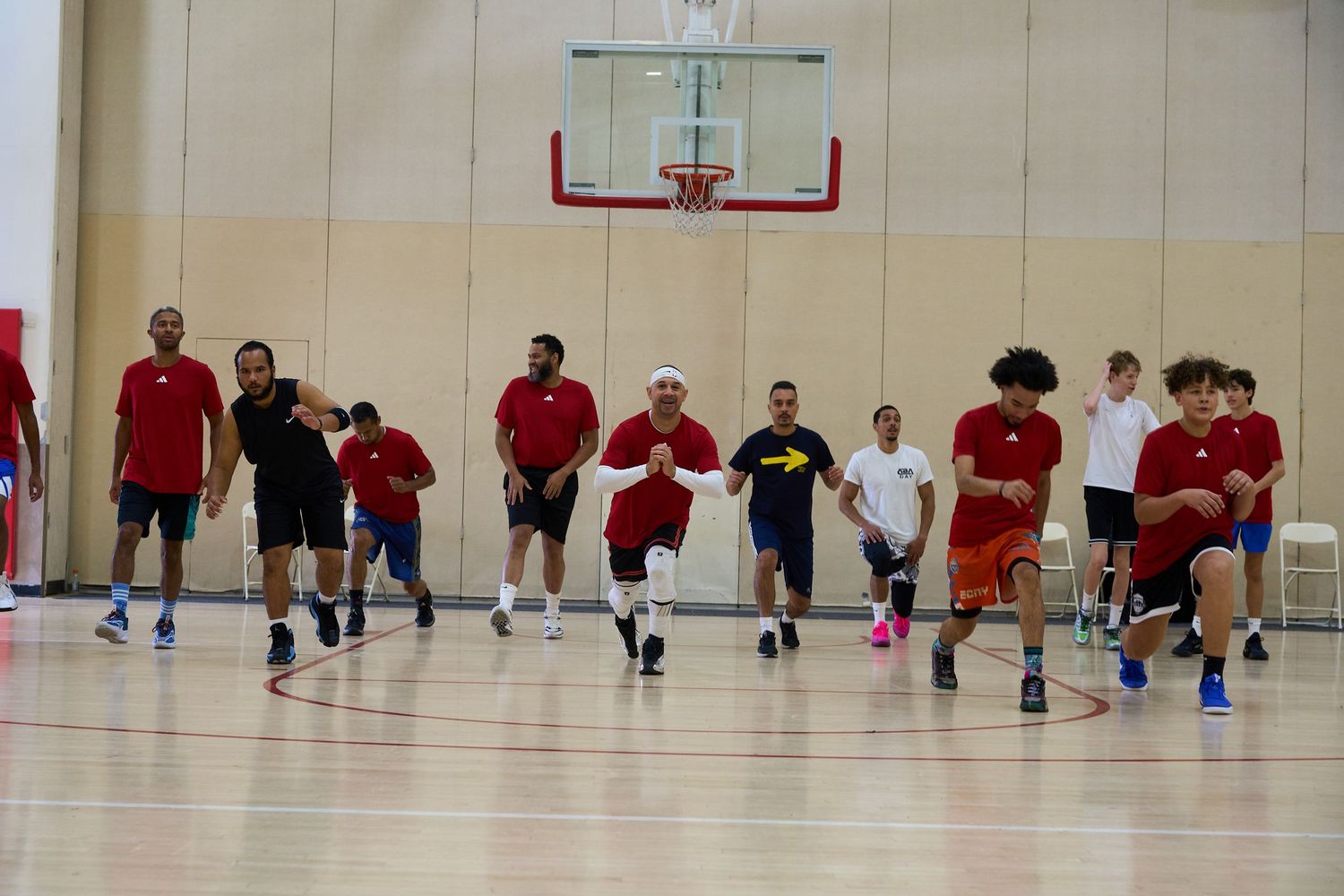 Athletes run in formation across a gymnasium floor during a basketball practice session.