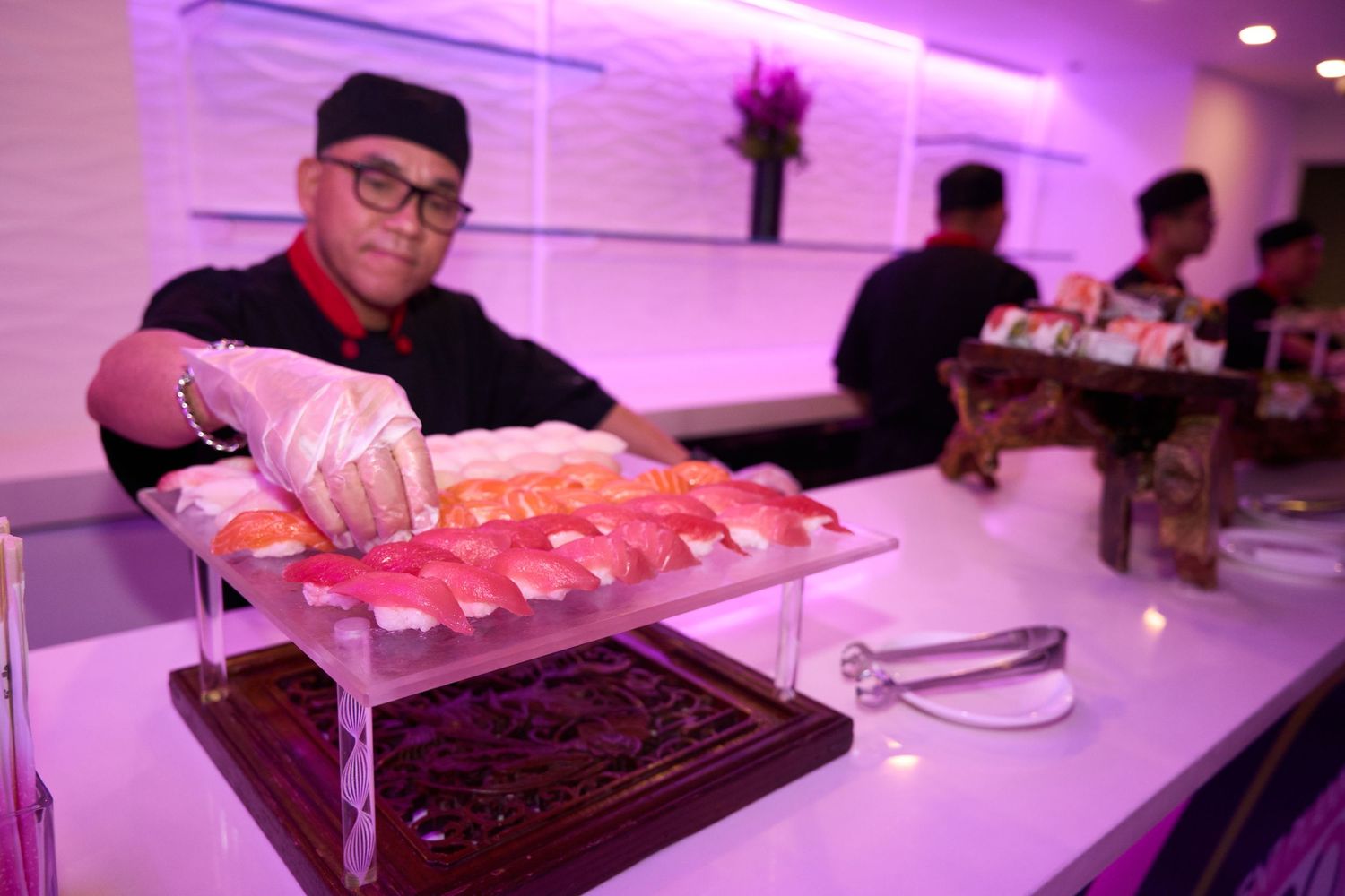 People seated at a long white table illuminated by pink and purple ambient lighting in a modern space.