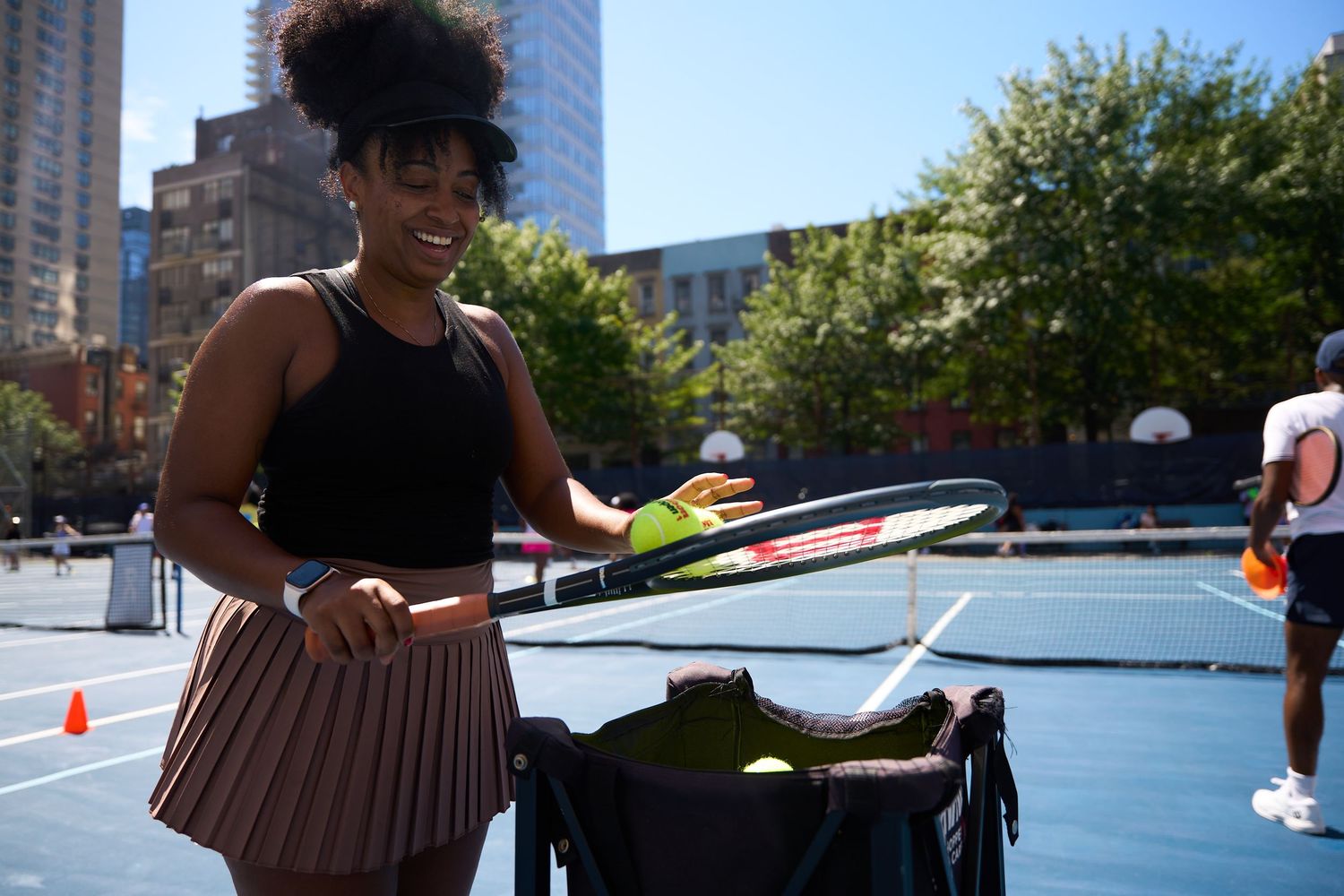 Tennis players practicing serves and drills on outdoor blue courts in an urban environment.