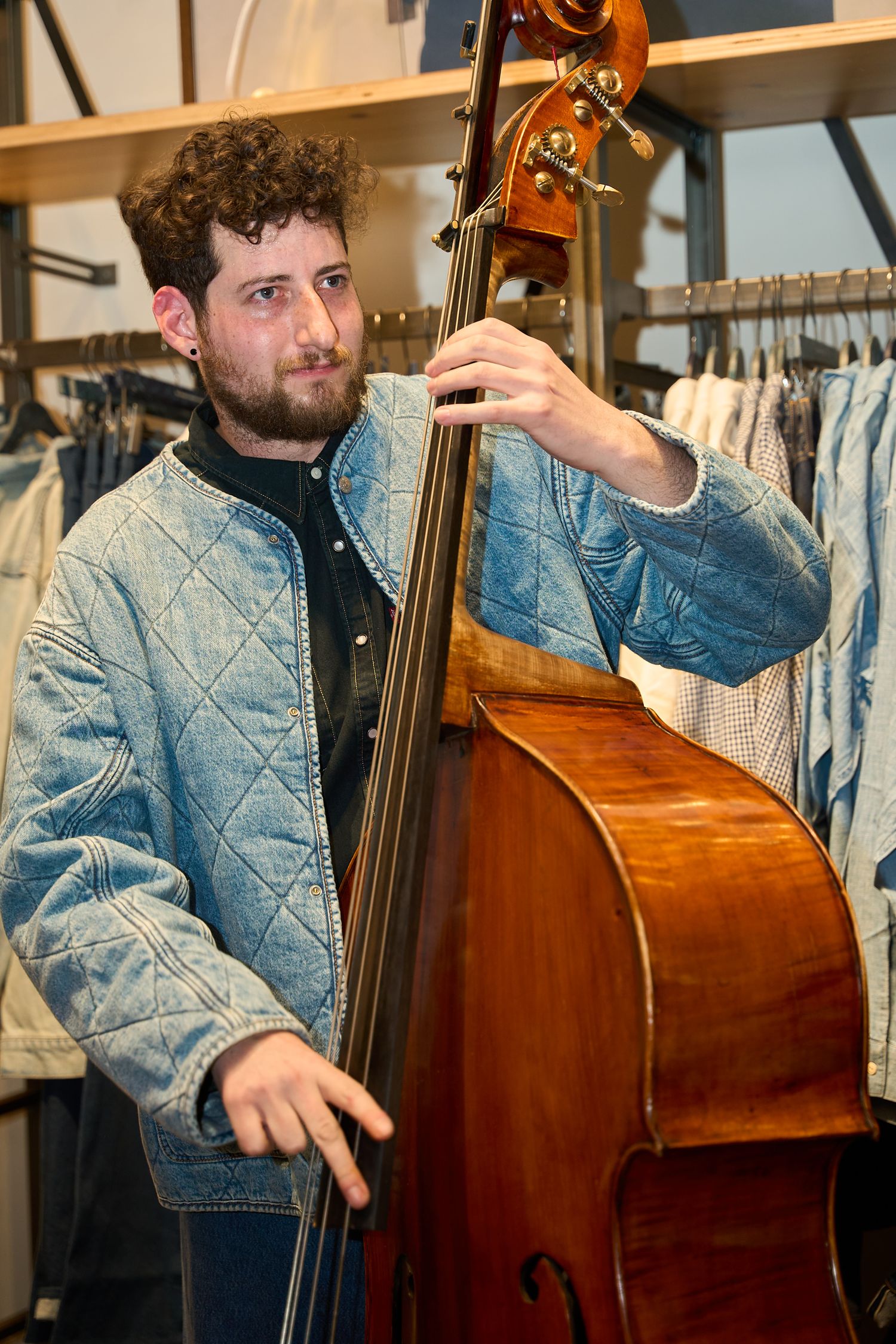 Musician in denim jacket plays upright bass during live performance at indoor venue.