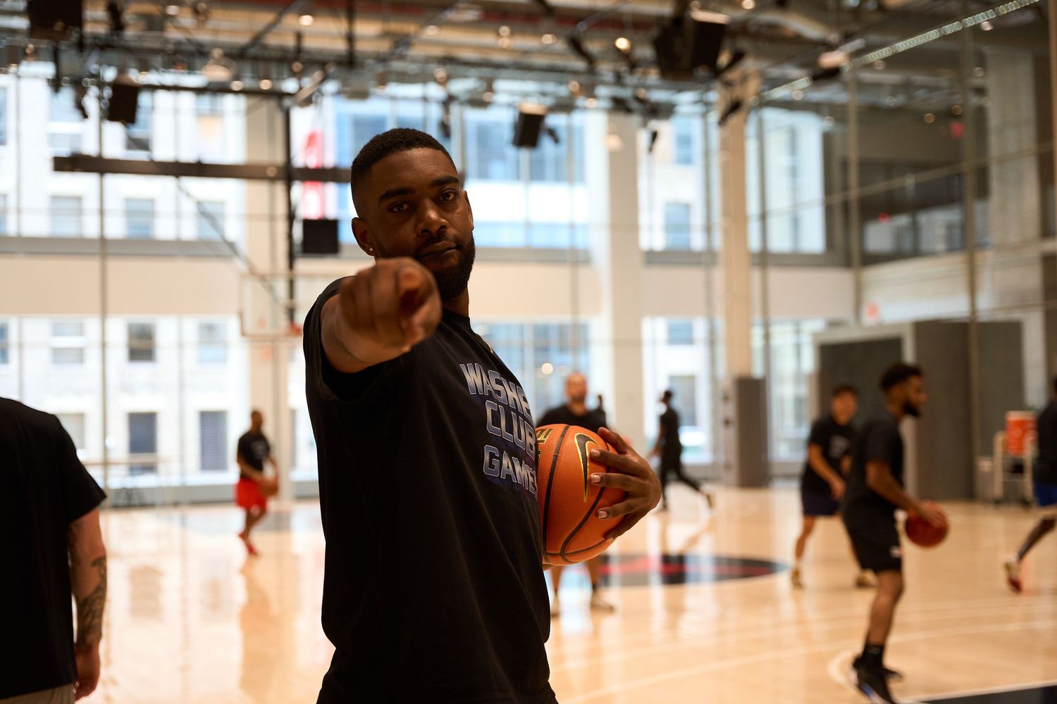 Basketball player points while holding a ball during practice in a modern indoor gymnasium.