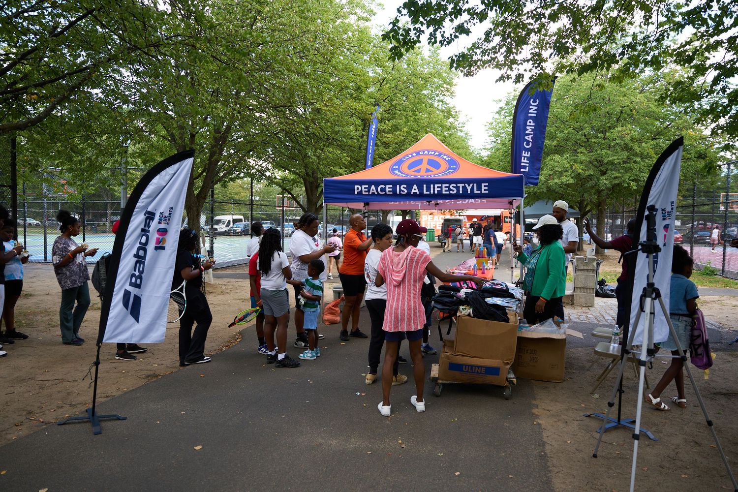 People mingling at an outdoor community event with tents and banners visible in a park setting.