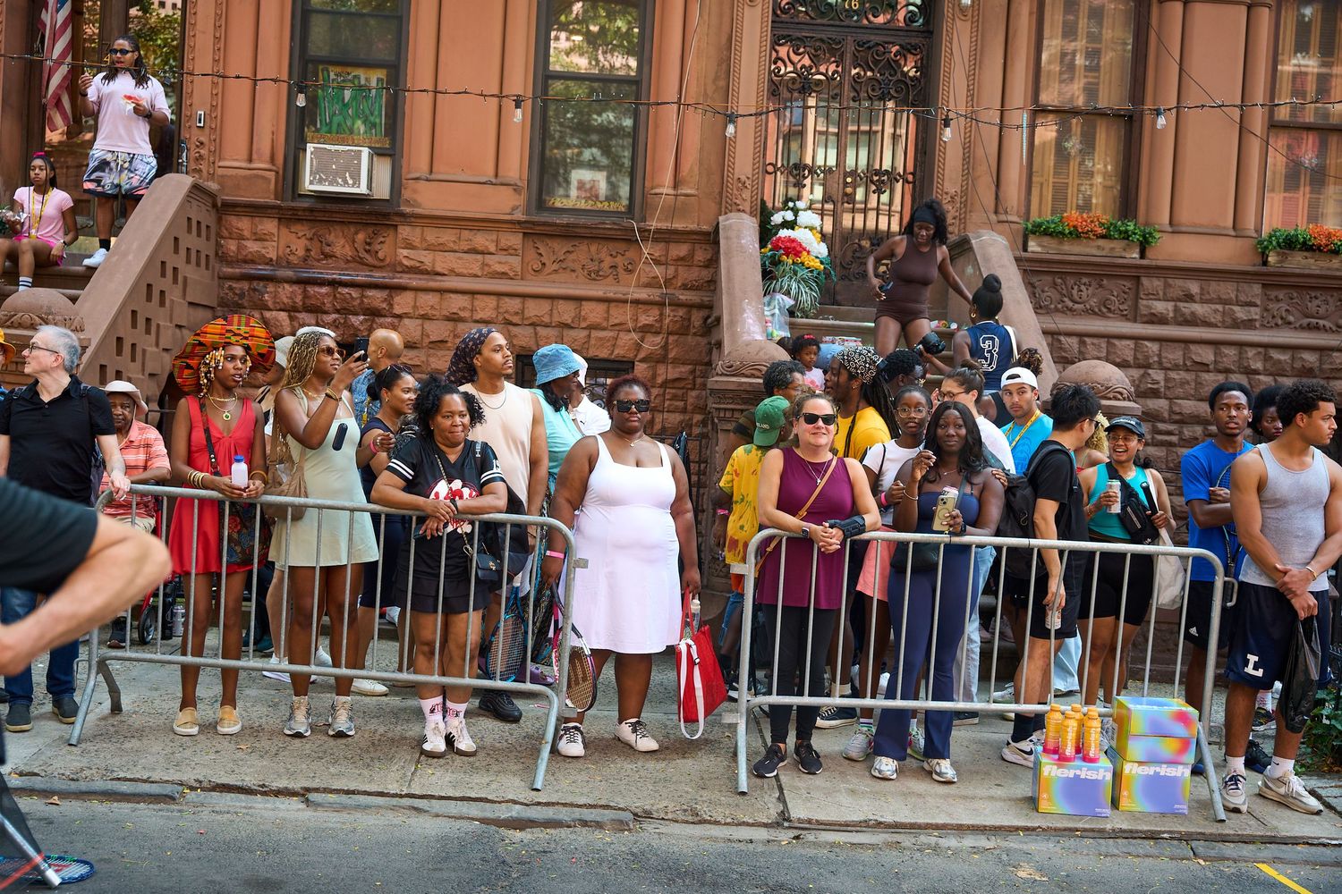 People gathered behind metal barriers on a city street during a summer event or celebration.