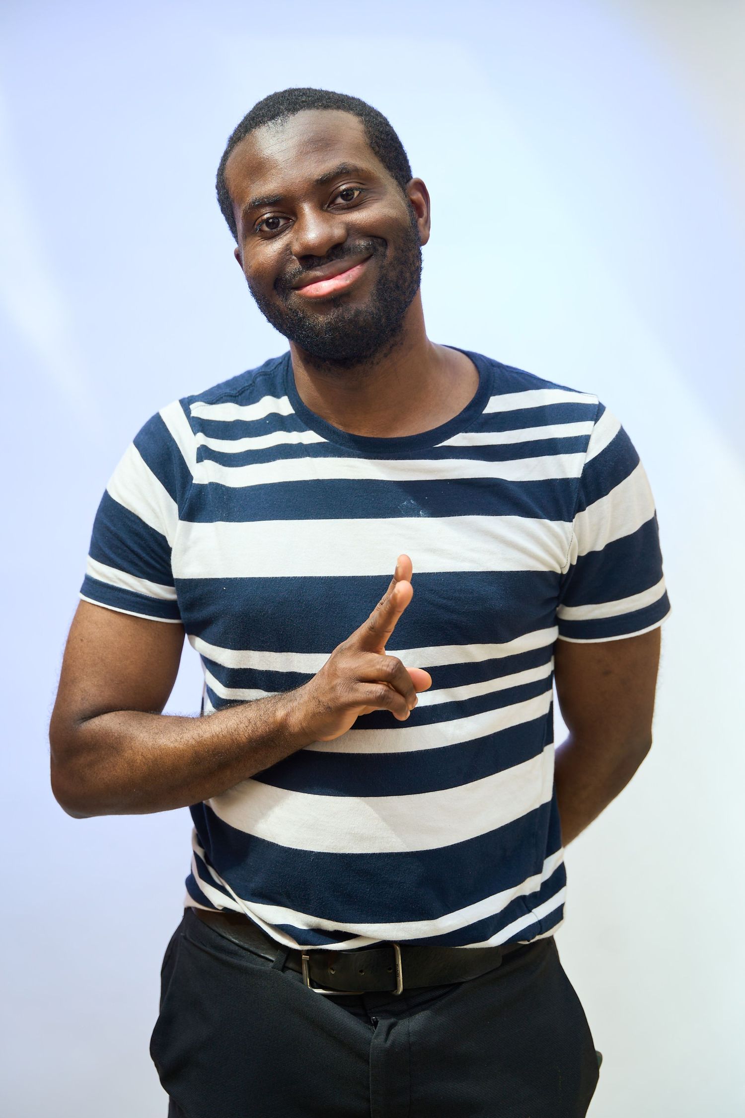 Smiling Black man in striped blue and white t-shirt pointing finger, posing against light background.