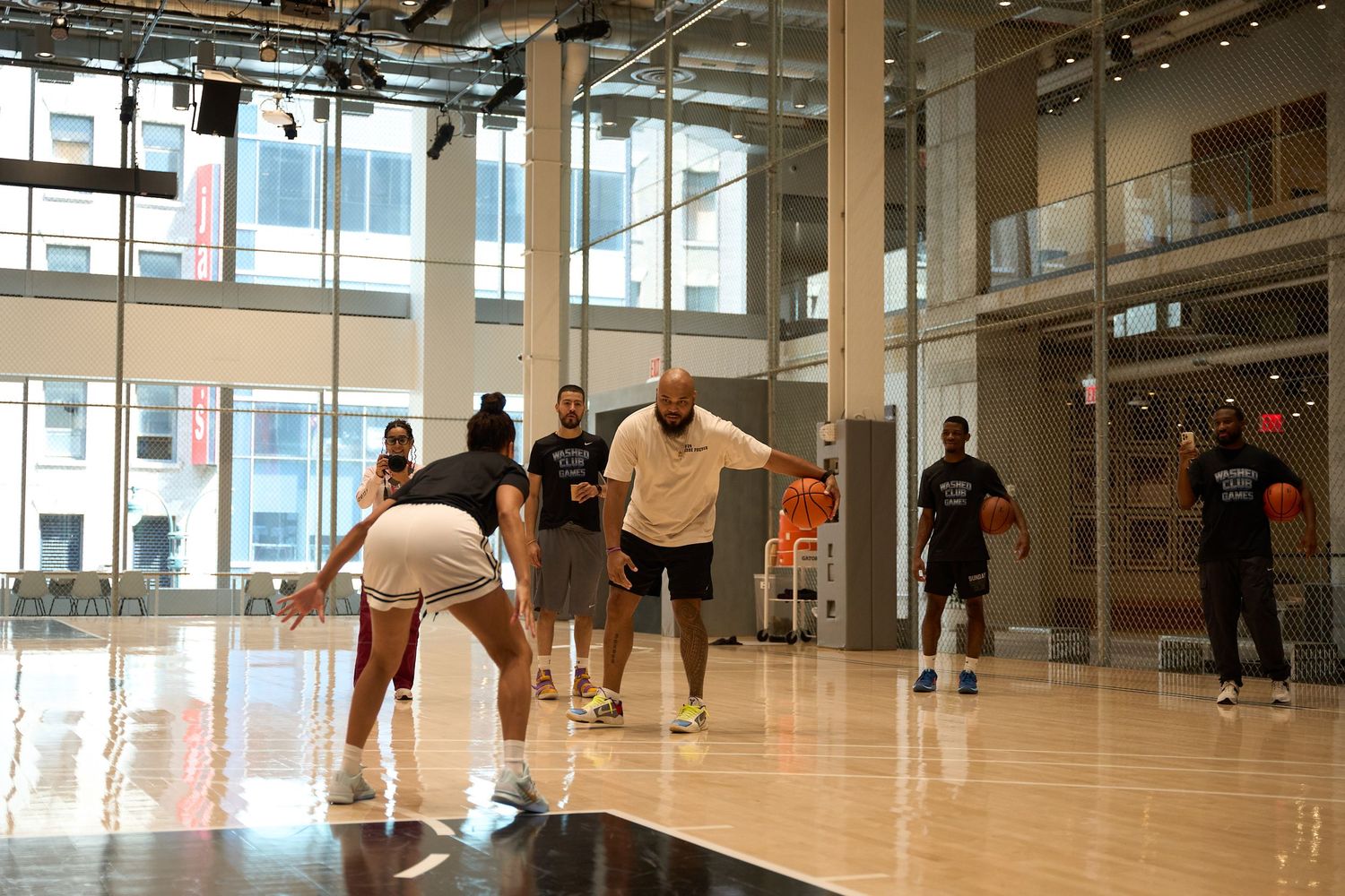 Students practicing in a bright indoor gym or dance studio with wooden floors and large windows.