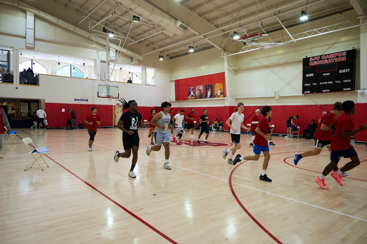 Basketball players practice drills on a red and white indoor court during a training session.