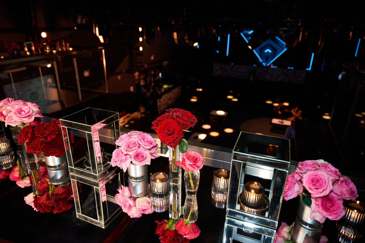 Pink and red roses arranged in glass vases illuminate a dark restaurant interior creating an elegant ambiance.