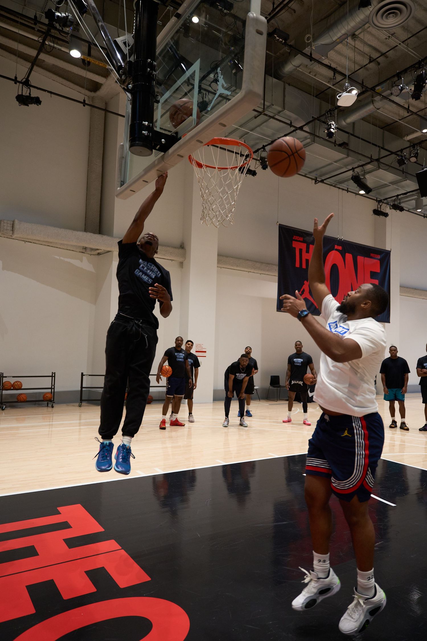 Basketball players practicing layups and drills on a modern indoor court with black flooring and white walls.
