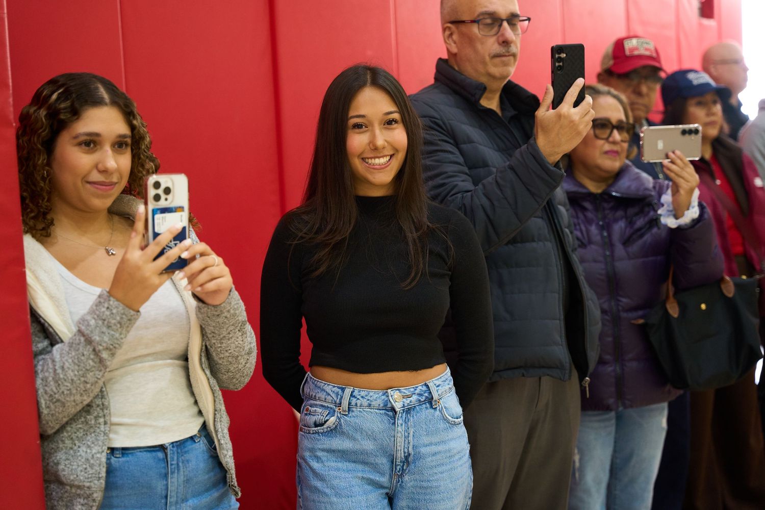 People lined up against red wall in gymnasium during an event.