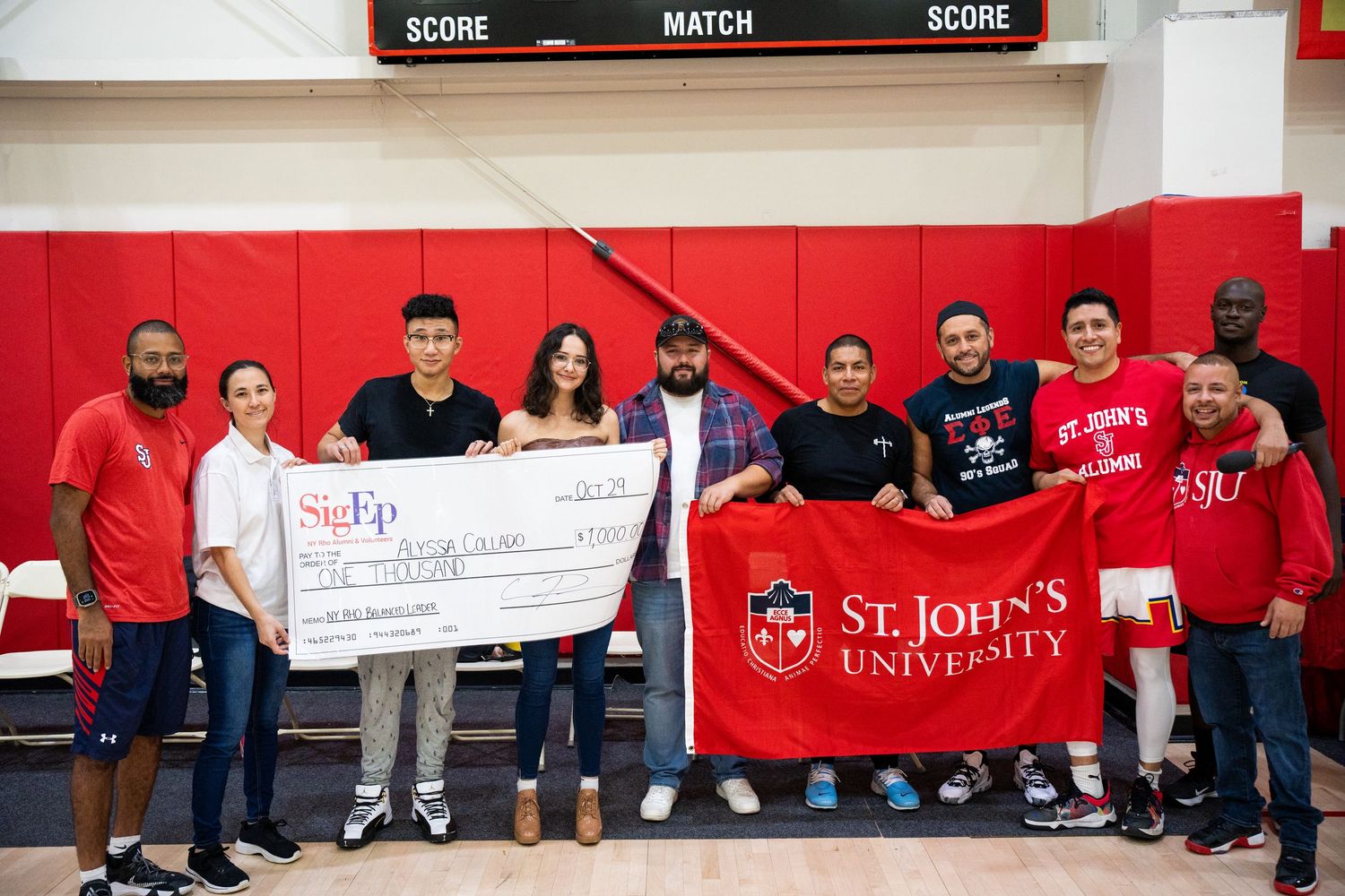 Group of people in red shirts holding large presentation checks at a university event.