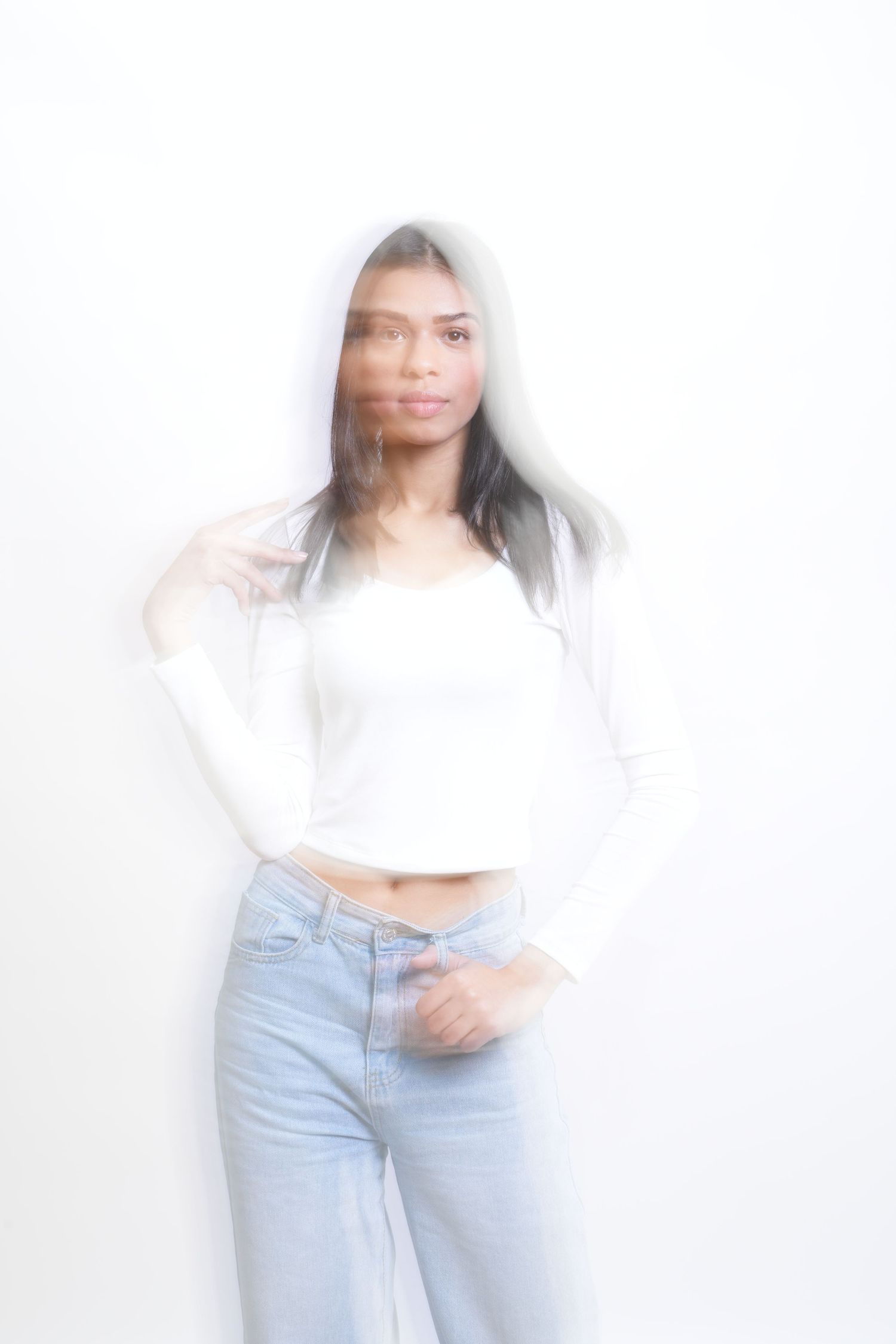 Artistic blurred portrait against white background showing figure in white crop top and light blue jeans.