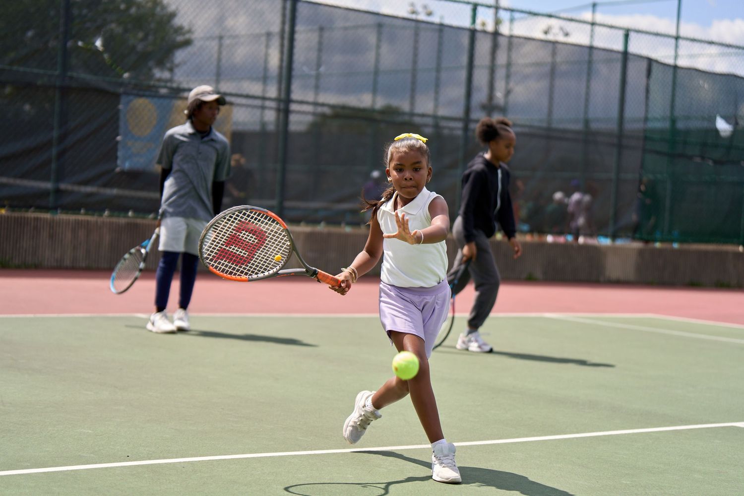 Players engaged in tennis drills and practice sessions on multiple outdoor courts during daytime.