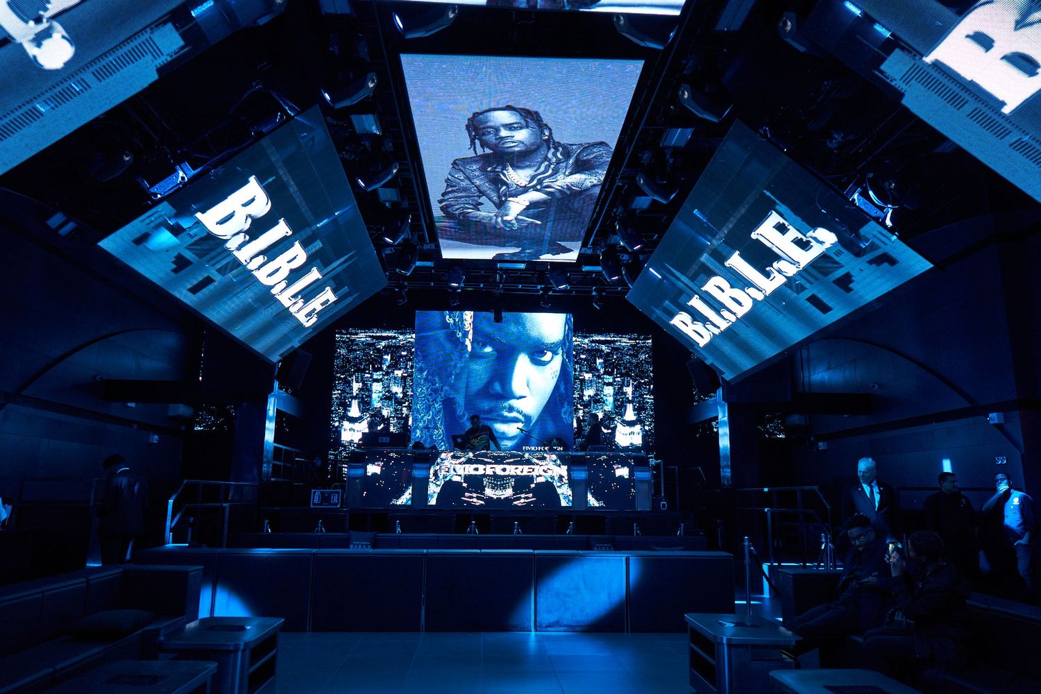 Concert venue illuminated in vibrant blue lighting with multiple screens and dynamic stage setup during performance.