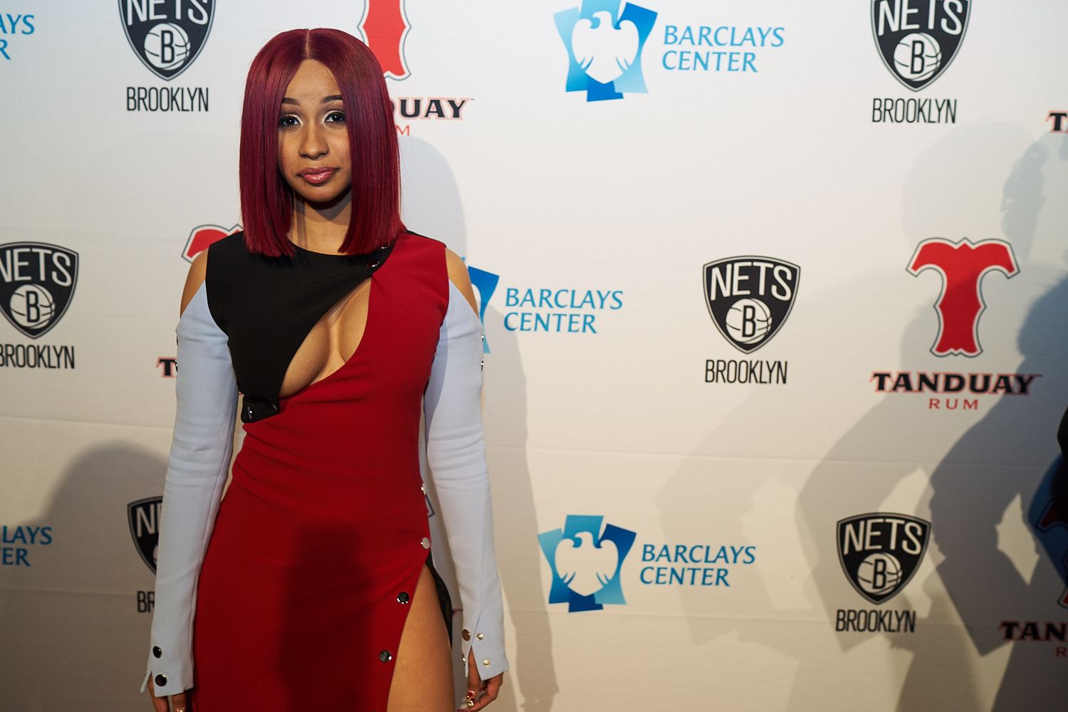 Attendee poses at media event with Brooklyn Nets branded backdrop and Barclays Center logos.