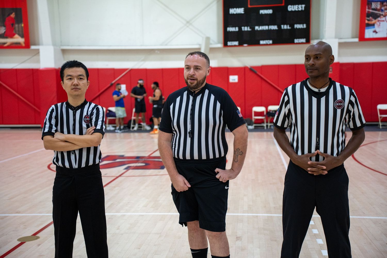Three basketball referees in black and white striped uniforms stand together on a court with red walls.