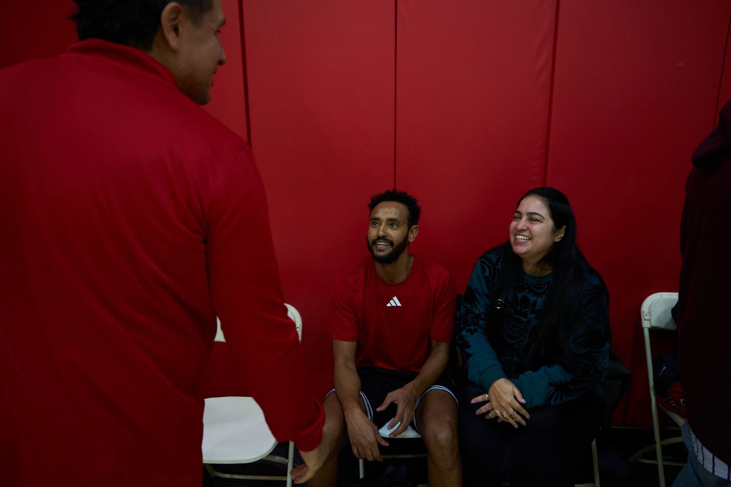 People having a conversation near a red wall in an indoor gymnasium setting.