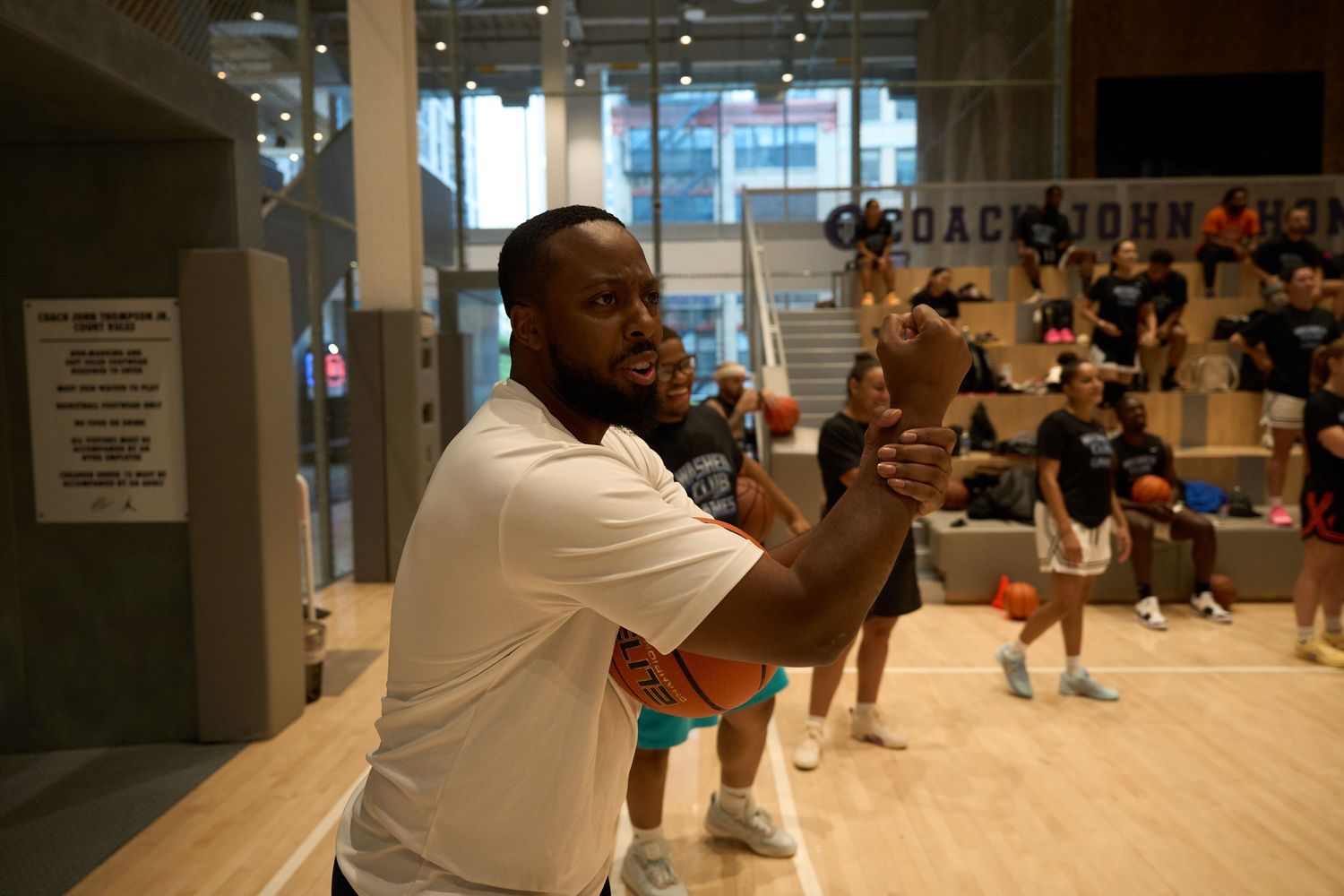 An instructor leads a fitness class in a modern gym studio with mirrors and wooden floors.