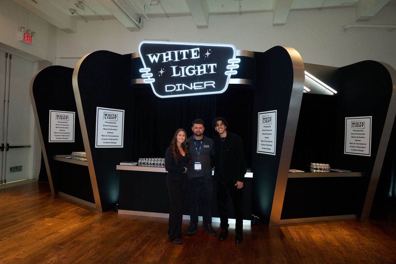 A black booth display with illuminated 'White Light Diner' signage set up in an indoor event space.