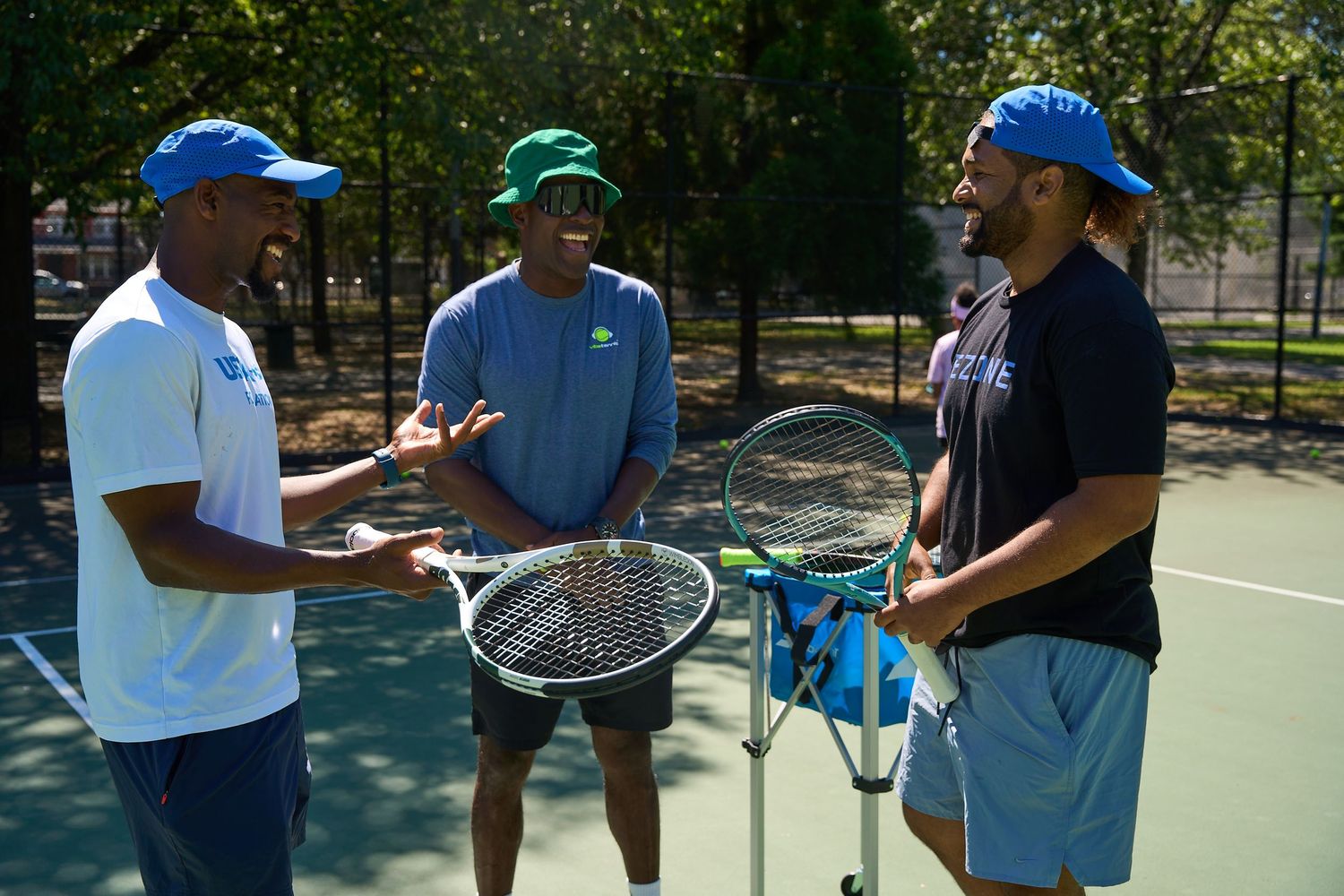 Three tennis players having a conversation on an outdoor court while holding rackets and wearing athletic gear.