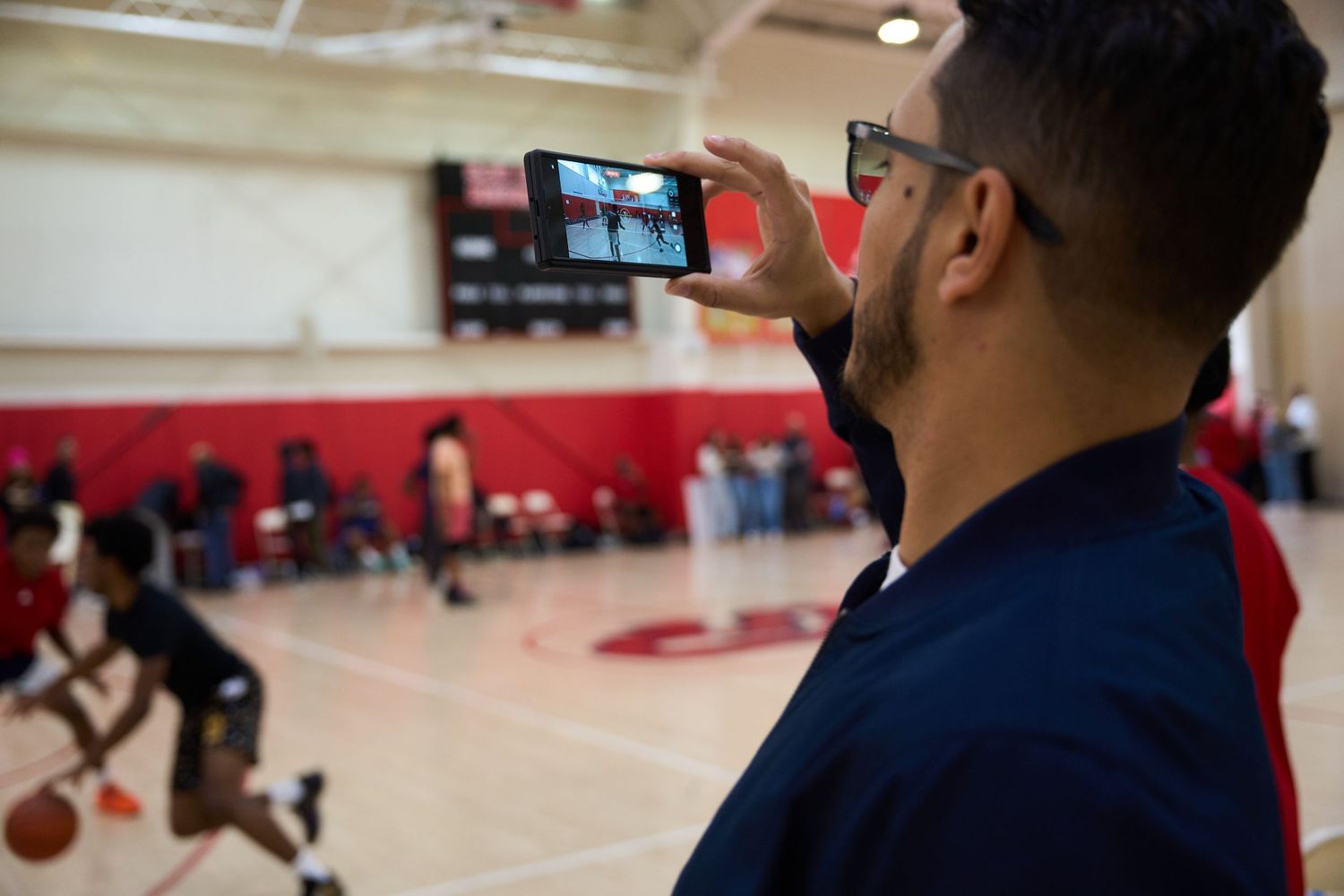 Basketball players practicing drills and skills on a gymnasium court with red walls.