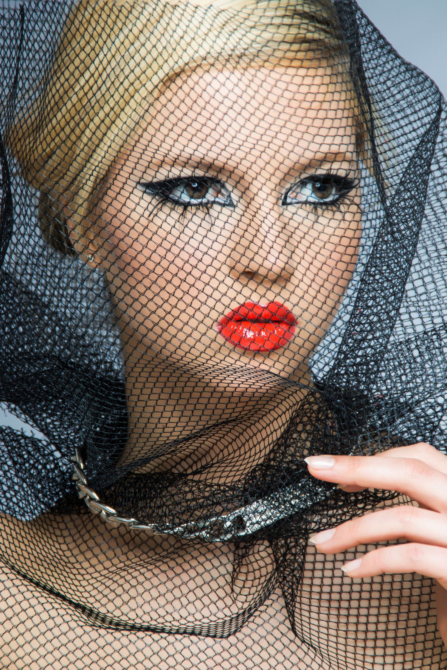 Close-up beauty portrait showing dramatic black mesh veil and bold red lipstick against pale complexion.