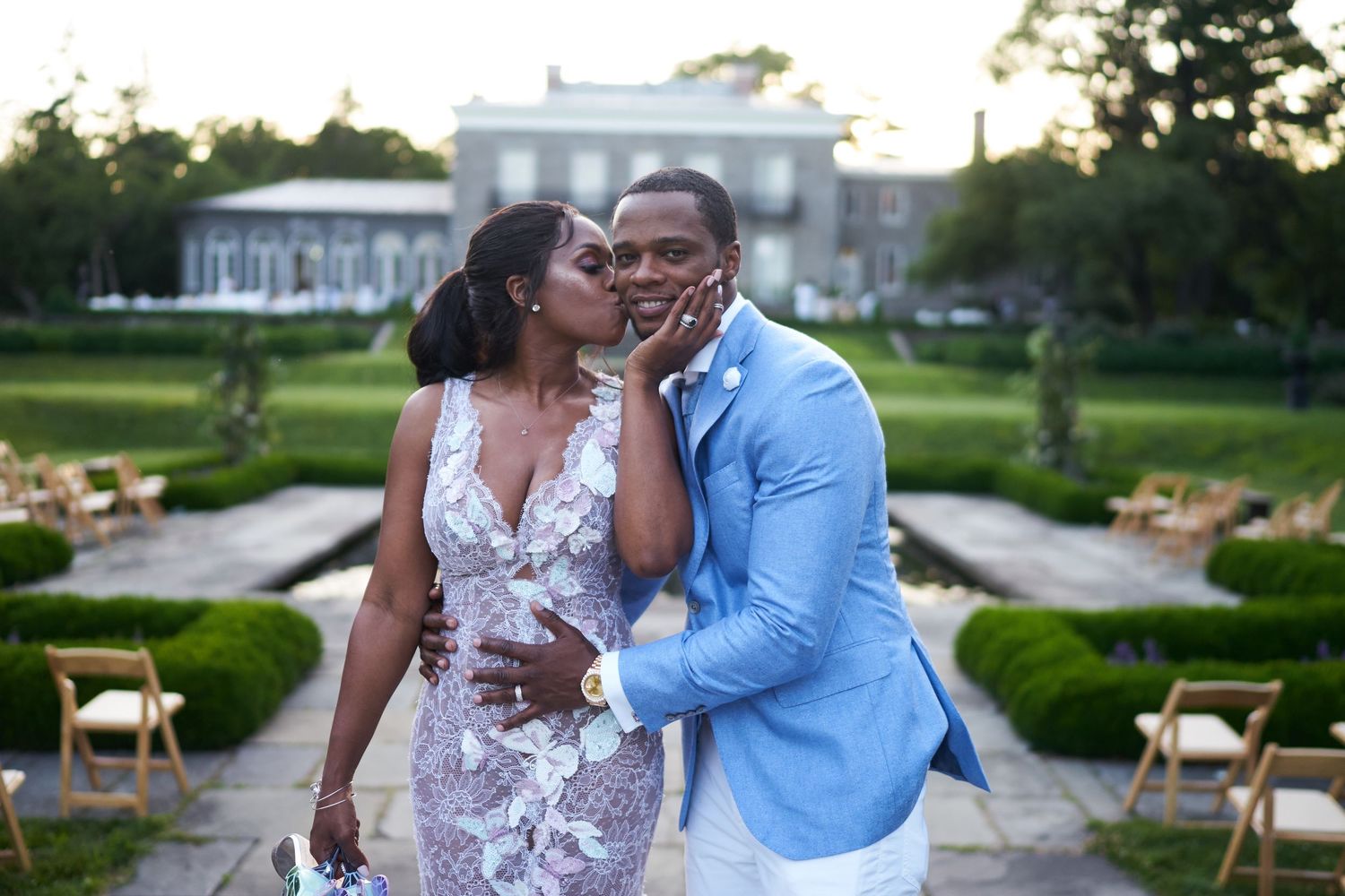 A joyful couple shares an intimate moment at an elegant garden wedding venue with white chairs setup outdoors.