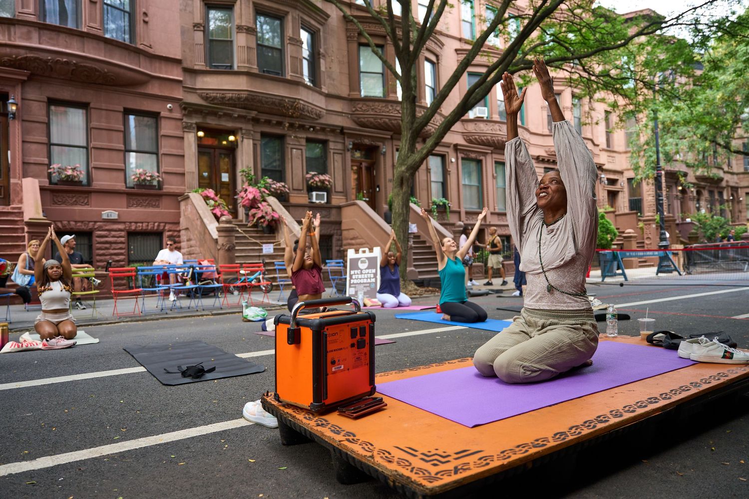 People practicing yoga on colorful mats along a brownstone-lined city street during an outdoor community event.