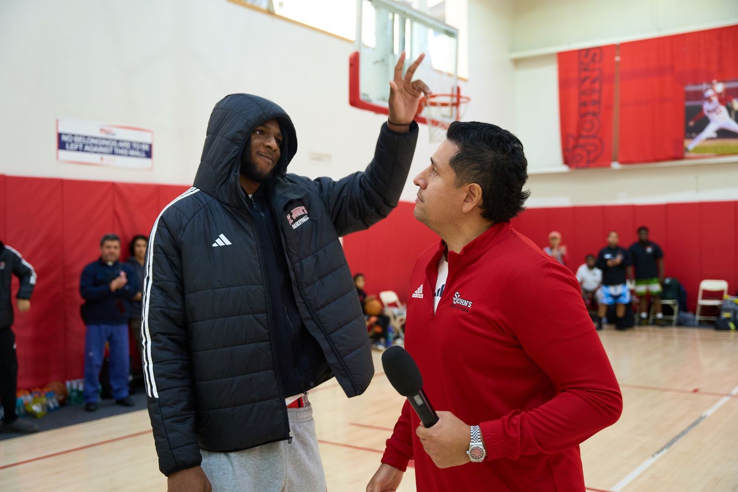 Two people interacting during a basketball training session in a gym with red walls.