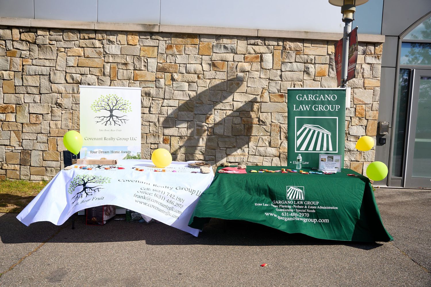 Stone wall display with green signs and yellow balloons at a community event.