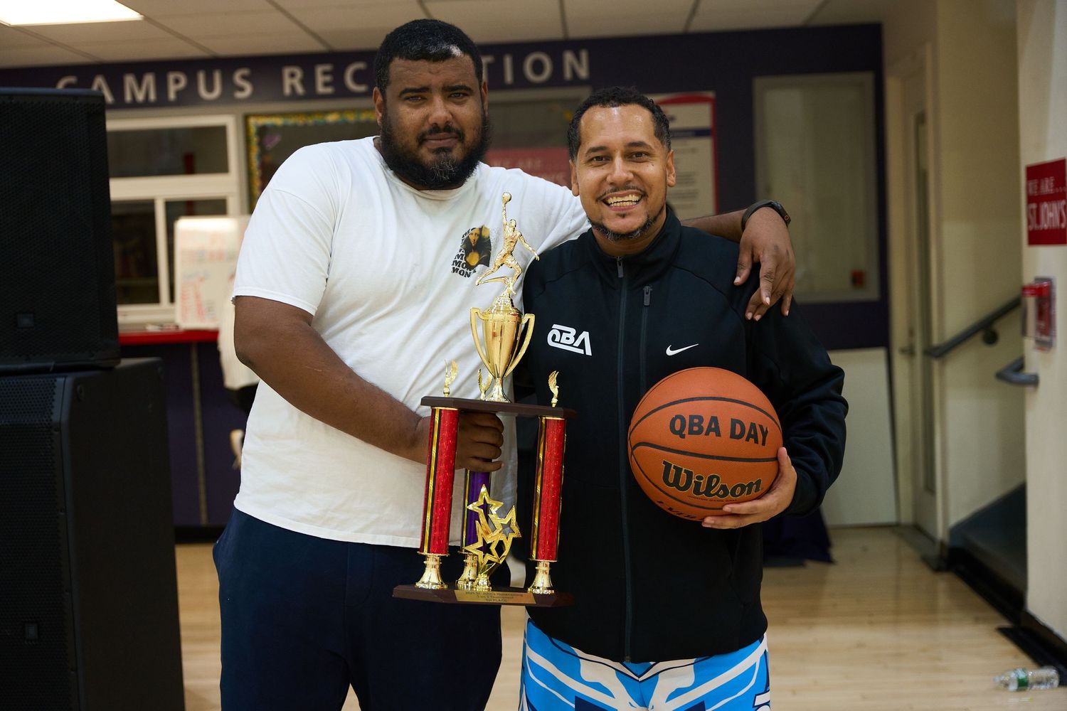 Two people posing with a trophy and basketball in front of a Campus Recreation sign.
